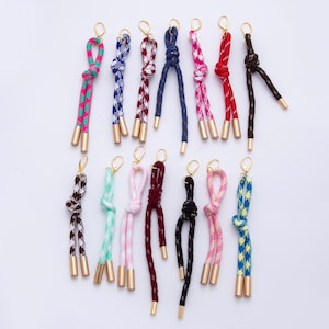 May include: A collection of colorful drawstring cords with gold-tone metal tips and clasps. The cords feature various patterns and colors, including pink, blue, red, and black. These decorative cords are ideal for crafting or fashion accessories.
