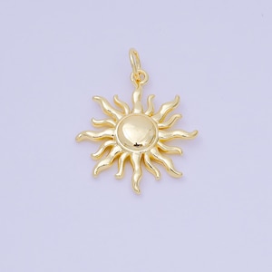 May include: A gold-colored sun pendant with a loop for hanging. The sun has a central disc with radiating wavy rays. The pendant is likely made of metal and is designed to be worn as jewelry.