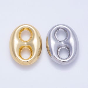 Puede incluir: Dos componentes de joyería de forma ovalada. Uno es de color dorado, el otro plateado. Cada uno tiene dos aberturas circulares. Los componentes tienen una superficie lisa y pulida sobre un fondo blanco.