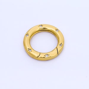 May include: A gold-colored, circular clasp with a hinged opening. The clasp is adorned with small, clear, star-shaped embellishments evenly spaced around the outer ring. The background is plain white.