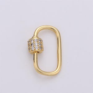 May include: A gold-colored, rectangular clasp with a cylindrical section encrusted with small, clear gemstones. The clasp is designed with a curved top and a straight bottom, suitable for jewelry making or crafts.