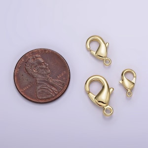 May include: Three gold-toned lobster clasps of different sizes. The clasps are shown next to a US penny for scale.