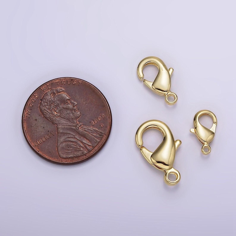 May include: Three gold-toned lobster clasps of different sizes. The clasps are shown next to a US penny for scale.
