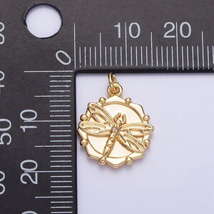 May include: Gold-toned pendant featuring a detailed dragonfly design with a clear rhinestone in the center. The pendant is approximately 1 inch in diameter and hangs from a gold-toned bail.