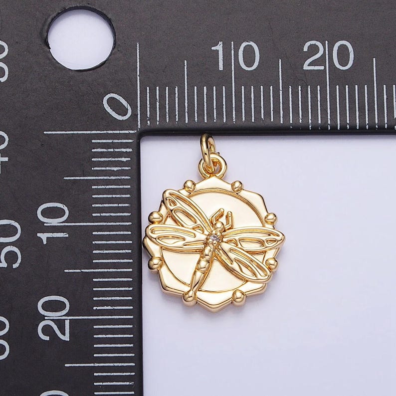 May include: Gold-toned pendant featuring a detailed dragonfly design with a clear rhinestone in the center. The pendant is approximately 1 inch in diameter and hangs from a gold-toned bail.