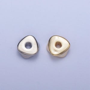 May include: Two triangle-shaped beads with a hole in the center. One bead is silver and the other is gold.