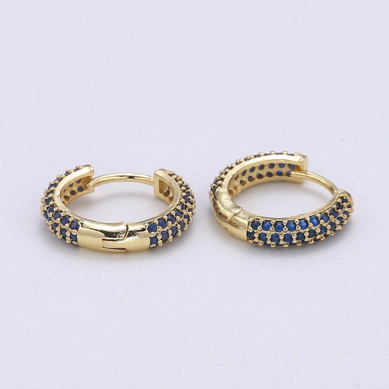 Pu&ograve; includere: Un paio di orecchini a cerchio color oro. Ogni orecchino &egrave; incastonato con piccole pietre preziose blu scuro. Gli orecchini hanno una chiusura a cerniera e una finitura liscia e lucida. Le pietre preziose sono uniformemente distanziate attorno ai cerchi.