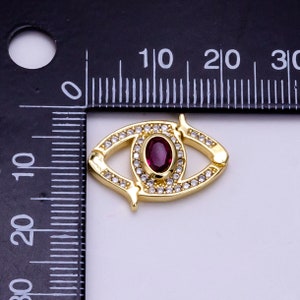 May include: Gold-tone eye charm with a red gemstone center and clear rhinestones around the eye and the perimeter. The charm is approximately 2 cm long.