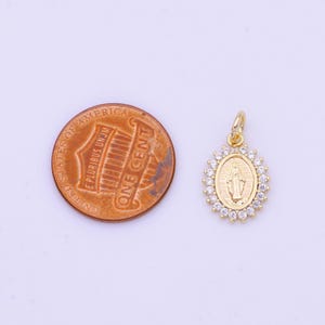 May include: Gold-tone pendant featuring a depiction of the Virgin Mary with a halo of clear cubic zirconia stones. The pendant is shown next to a US penny for size comparison.