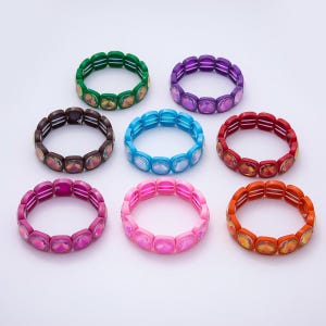 Può includere: Una collezione di otto braccialetti elastici disposti in un motivo circolare. Ogni braccialetto presenta perline di vetro quadrate, sfaccettate e iridescenti in vari colori, tra cui verde, viola, marrone, blu, rosso, magenta, rosa e arancione.