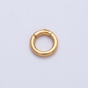 May include: A gold-colored, circular clasp with a hinged opening. The clasp is a solid, rounded shape, designed to secure jewelry or other accessories. The metal has a polished finish, reflecting light.