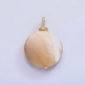 May include: A gold pendant with a round, cream-colored shell and a clear crystal halo around the bail.