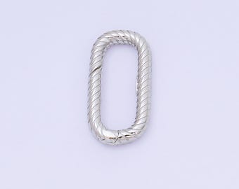 May include: A silver-colored, oval-shaped jewelry link. The link has a textured, ridged design along its outer edges. The clasp is visible at the bottom of the link. The background is a solid, light color.