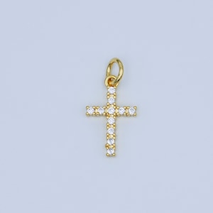 May include: A gold-colored cross pendant with a loop at the top for a chain. The cross is encrusted with small, clear gemstones. The pendant is displayed against a light background.