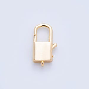 Peut inclure: Un fermoir rectangulaire de couleur or avec un dessus incurvé et un petit levier sur le côté. Le fermoir est conçu pour sécuriser des bijoux ou d'autres petits objets. Le fond est de couleur claire unie.