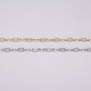 May include: Two delicate necklaces, one gold-toned and one silver-toned, each featuring rectangular, clear gemstones. The gemstones are evenly spaced along the chain, creating a refined and elegant look. The chains are displayed against a neutral background.