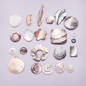 May include: A collection of iridescent shell pendants and beads in various shapes, including leaves, flowers, and spirals. The color palette includes white, gold, and shades of gray. These decorative elements are ideal for jewelry making and craft projects.