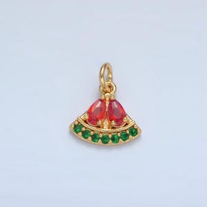 Puede incluir: Colgante dorado con forma de rodaja de sandía con piedras preciosas rojas y verdes. El colgante presenta una gema roja en forma de lágrima en la parte superior y una fila de gemas verdes en el borde inferior. Diseñado como una joya.