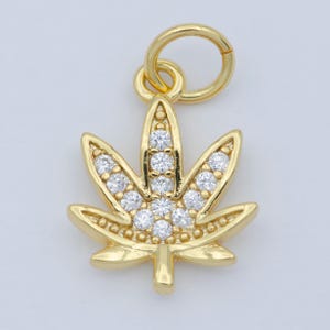 May include: A gold-toned pendant charm in the shape of a marijuana leaf with clear cubic zirconia stones.