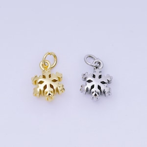 May include: Two snowflake charms, one gold-colored and one silver-colored, are displayed against a white background. Each charm has a loop at the top for attaching to a necklace or bracelet. The snowflake design is detailed and three-dimensional.