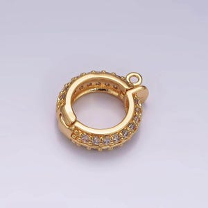 Könnte beinhalten: Goldfarbener Metallverschluss mit runder Form und einer Reihe von klaren Strasssteinen am Rand.