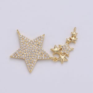 Puede incluir: Pendiente de tono dorado con una gran estrella adornada con brillantes transparentes y una cadena más pequeña de estrellas con brillantes transparentes.