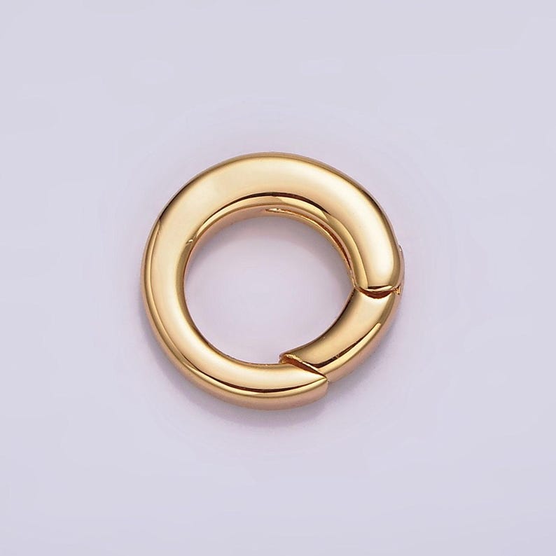 Pode incluir: Um anel de metal dourado com uma superf&iacute;cie lisa e arredondada. O anel &eacute; aberto de um lado e tem um fecho com dobradi&ccedil;a.