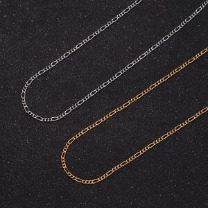 May include: Two gold and two silver chain necklaces on a black background. The chains are all the same style, with a delicate, oval-shaped link.
