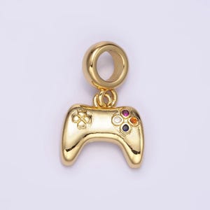 May include: A gold-colored charm in the shape of a video game controller with colorful gemstones on the buttons. The charm has a loop at the top for attaching to a bracelet or necklace.