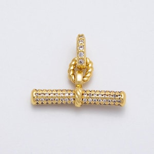 May include: A gold-colored toggle clasp with a bar and ring design. The bar and ring are encrusted with small, clear gemstones. The clasp features a twisted rope design connecting the bar and ring.