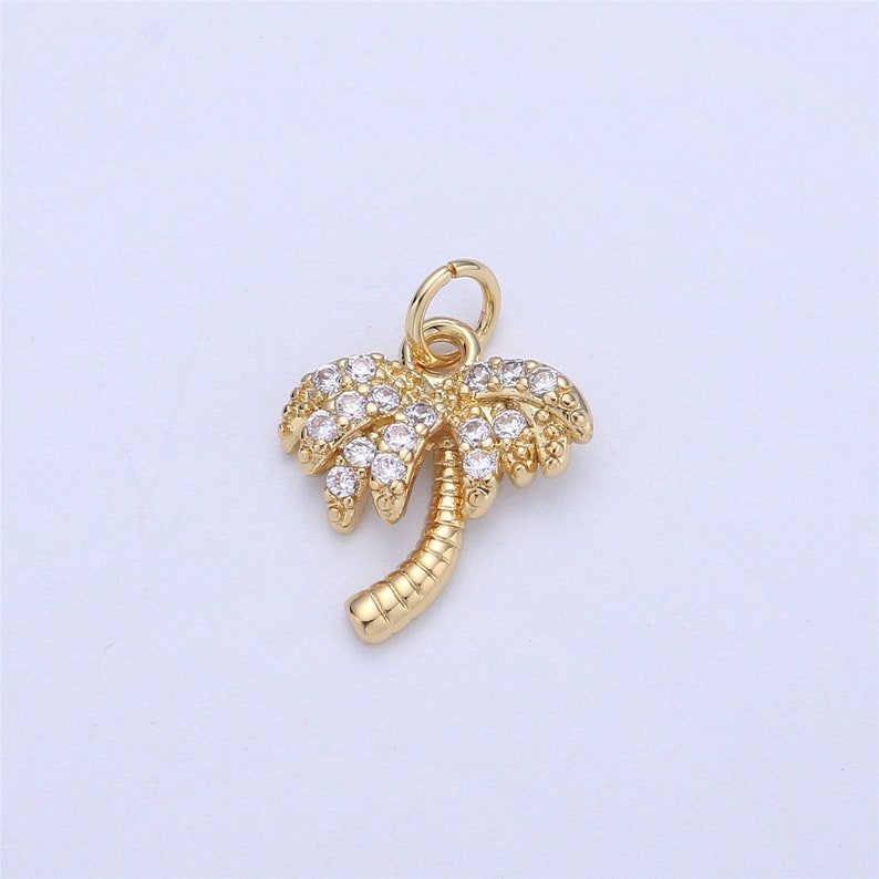 May include: Gold palm tree charm with clear crystal accents. The charm has a loop at the top for attaching to a necklace or bracelet.