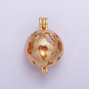 May include: Gold-toned metal charm with a spherical, openwork design. The charm has a textured surface and features small, clear rhinestones.