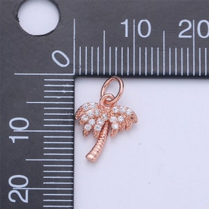 May include: A rose gold palm tree charm with clear cubic zirconia stones. The charm is approximately 1 cm in size and has a loop at the top for attaching to a bracelet or necklace.