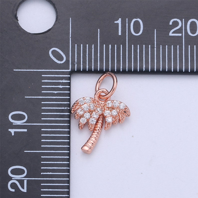 May include: A rose gold palm tree charm with clear cubic zirconia stones. The charm is approximately 1 cm in size and has a loop at the top for attaching to a bracelet or necklace.