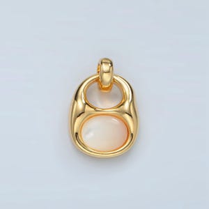 Puede incluir: Un colgante de oro con una piedra ovalada blanca en el centro. El colgante tiene forma de círculo con un círculo más pequeño cortado en la parte superior.