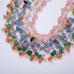 May include: A collection of colorful gemstone necklaces. Each necklace features a strand of irregularly shaped stones in shades of pink, blue, green, orange, and purple, strung on gold-colored wire. The necklaces are arranged in a layered, cascading design.
