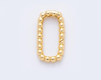 May include: A gold-coloured, oval-shaped clasp. The clasp is made of small, rounded beads connected together. The beads have a shiny, reflective surface. The clasp is set against a white background.