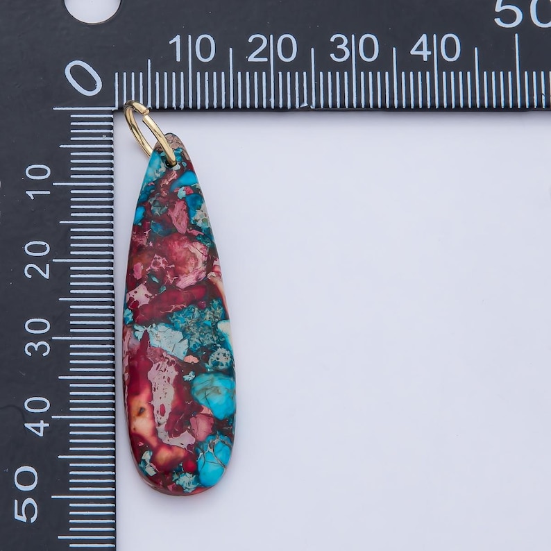 May include: A teardrop-shaped pendant with a gold-colored bail. The pendant is made of a stone with a mix of red, blue, and cream colors. The pendant is approximately 1.5 inches long.