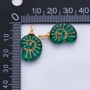 May include: Two green glass pendants with a spiral design and gold-colored metal findings. The pendants are approximately 0.75 inches in diameter. The design is reminiscent of a nautilus shell. Ideal for jewelry making.