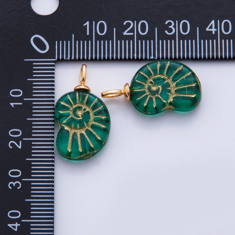 May include: Two green glass pendants with a spiral design and gold-colored metal findings. The pendants are approximately 0.75 inches in diameter. The design is reminiscent of a nautilus shell. Ideal for jewelry making.