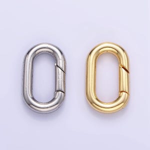 May include: Two oval-shaped metal clasps, one silver and one gold. The clasps are open and ready to be attached to a chain or other jewelry.