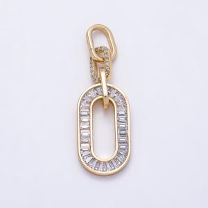 May include: A gold-toned pendant featuring a large oval link encrusted with clear baguette-cut stones, connected to a smaller oval link paved with tiny round clear stones, and topped with a plain gold-toned oval bail for attachment to a chain.
