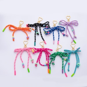 May include: A collection of colorful keychains in various colors, including orange, black, blue, purple, pink, and green. Each keychain features a heart-shaped clasp and decorative cord details with colorful accents.