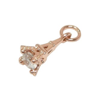 May include: A rose gold charm in the shape of the Eiffel Tower with a clear crystal at the top. The charm has a loop at the top for attaching to a bracelet or necklace.