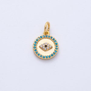May include: A gold-colored round pendant with a turquoise border and a central eye design. The eye features a black center and is surrounded by small white stones. The pendant has a loop for attaching to a chain or bracelet.