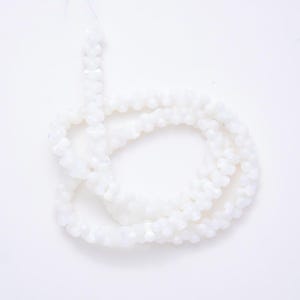 May include: A single strand of small, opaque white beads arranged in a loose, circular coil. Each bead features a uniform, rounded shape with a smooth, matte finish, strung together on a thin, barely visible thread against a plain white background.