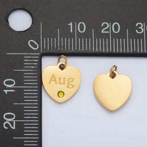 May include: Two gold heart-shaped charms, one with the word "Aug" engraved and a small green rhinestone, the other plain.
