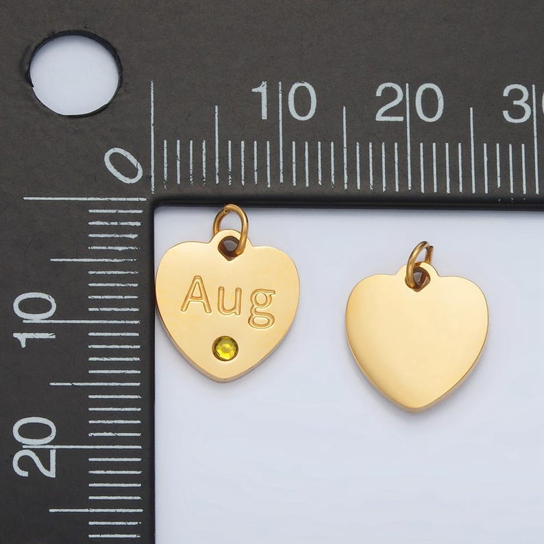 May include: Two gold heart-shaped charms, one with the word "Aug" engraved and a small green rhinestone, the other plain.
