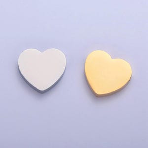 Puede incluir: Dos dijes de metal en forma de coraz&oacute;n, uno plateado y otro dorado. Los dijes son lisos y tienen un acabado brillante.