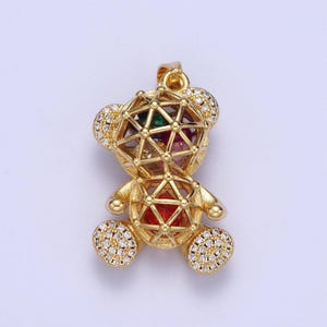 May include: A gold-tone pendant featuring a teddy bear design with a cage-like center filled with colorful gemstones. The bear is adorned with clear cubic zirconia stones.